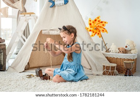 Little girl exploring jewellery from small chest sitting on room's floor in front of wigwam