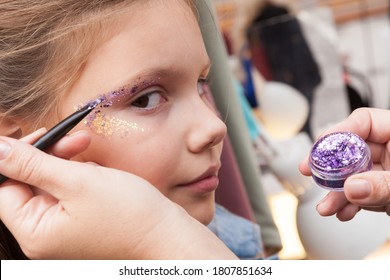 Little girl face makeup applying with colorful glitter