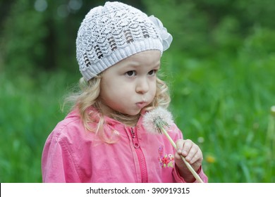 Little Girl With Fair Hair Blowing On White Dandelion Seed Head