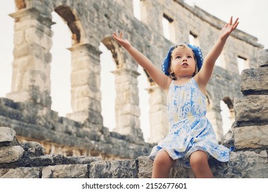 Сute little girl with family exploring Roman Amphitheater Arena like as Coliseum - famous tourist travel destination in Pula, Croatia. A child plays in historical ruins of an ancient structure