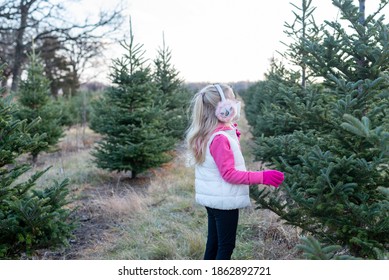 Little Girl In Fashionable Earmuffs And Face Mask At The Christmas Tree Farm