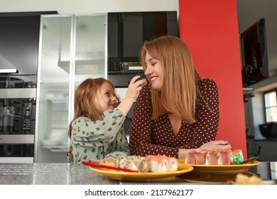 Little Girl Feeding Her Mother Sushi With Chopsticks Close Up. Food Takeout And Delivery Service, Salmon Sushi Rolls.