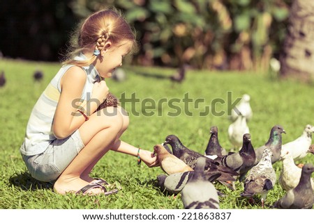 little girl feeding pigeons in the park at the day time