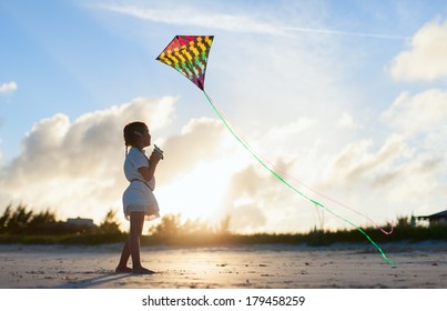 Little Girl Flying A Kite On Beach At Sunset