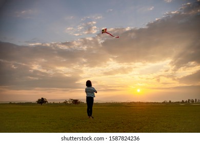Little girl flying a kite at sunset - Shutterstock ID 1587824236