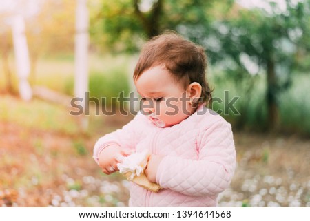 little girl in the garden on the background of greenery and trees very cute eating ice cream finger in a waffle Cup dirty face
