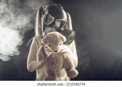 Little girl in a gas mask in smoke with a bear in her arms on a black background. Air pollution, respiratory disease.