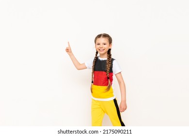 A little girl with a German flag on a T-shirt, with long hair in pigtails, points up with her index finger at your advertisement on a white isolated background. Language courses.