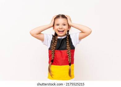 A little girl with a German flag on her T-shirt, with long hair braided into pigtails, clutching her gulova with two hands, smiling broadly on a white isolated background. Language courses. 