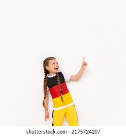 A little girl with a German flag on a T-shirt, with long hair in pigtails, points up with her index finger at your advertisement on a white isolated background. Language courses.
