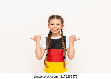 A little girl with a German flag on a T-shirt, with long hair in pigtails, points up with her index finger sideways at your advertisement on a white isolated background. Language courses.