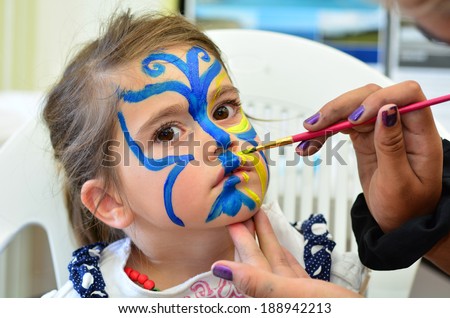 Little girl getting her face painted in butterfly shape by face painting artist. Make up. Real people. Copy space