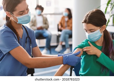 Little Girl Getting Vaccinated Against Covid, Female Doctor Applying Plaster After Giving Coronavirus Antiviral Vaccine Injection Shot Against Corona Virus Sitting In Health Centre Wearing Face Mask