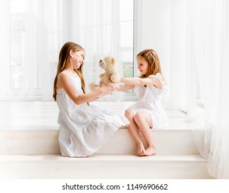 Little girl giving her teddy bear toy to older sister. Cute child girl giving a gift for her sister. Child girl sharing toy with friend