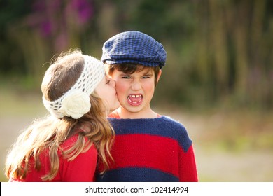 little girl giving kiss to young embarrassed boy.
