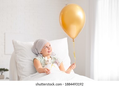 Kleines Mädchen mit goldenem Ballon, das Chemotherapie in der Klinik durchläuft. Sensibilisierungskonzept für Krebs im Kindesalter