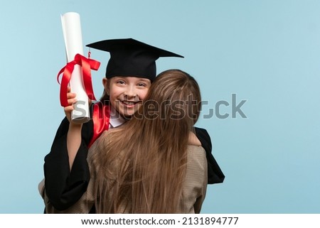 Little girl graduate celebrating graduation. Child wearing graduation cap and ceremony robe Holding Certificate. Mom hugs and congratulations daughter on graduation. Successfully complete course study