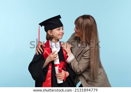 Little girl graduate celebrating graduation. Child wearing graduation cap and ceremony robe Holding Certificate. Mom hugs and congratulations daughter on graduation. Successfully complete course study