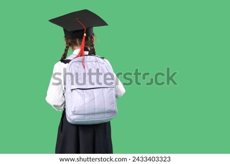 Little girl in graduation hat with backpack on green background, back view. End of school year