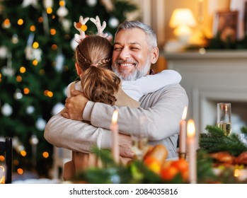 Little girl granddaughter hugging embracing happy smiling grandfather during Christmas festive dinner at home, grandchild thanking to grandpa for xmas present while celebrating New Years Eve together - Powered by Shutterstock