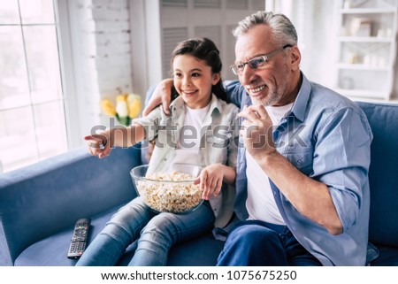 The little girl and a grandfather wathing television with a popñorn