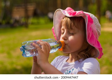 A Little Girl Greedily Drinking Water From A Bottle In Hot Weather In Summer