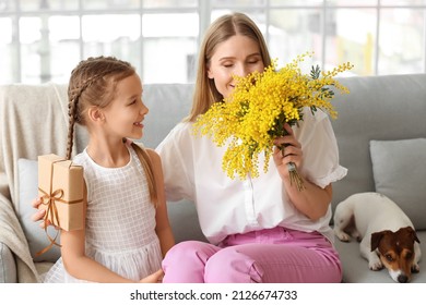 Little girl greeting her mother with mimosa flowers and gift at home on holiday