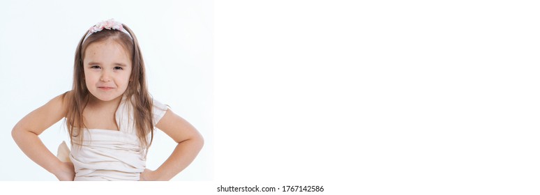 a little girl grimaces against a white background. The child looks sternly at the camera