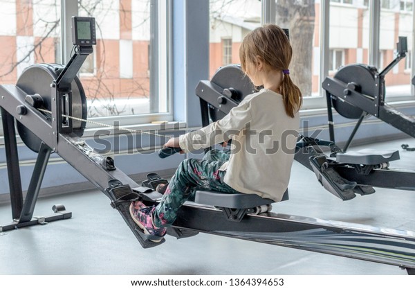 Little girl in the gym rowing club sitting\
on the rowing Ergometer. academic rowing for children, preparation\
for competitions