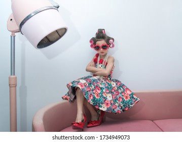 Little girl with hair curlers and red sunglasses sitting on couch, near the old style hair dryer, Kid's fashion - Powered by Shutterstock