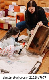 Little Girl With Hammer In Hands Fixing Old Wooden Box And Mother Holding Box Firmly In Workshop For Renovation. Giving Old Things New Life. Reuse Of Aged. Sustainable Actions For Helping Planet.