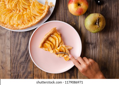 Little Girl Hands Eating A Portion Of Apple Pie Tart On A Pink Dish On Rustic Wooden Background. Top View