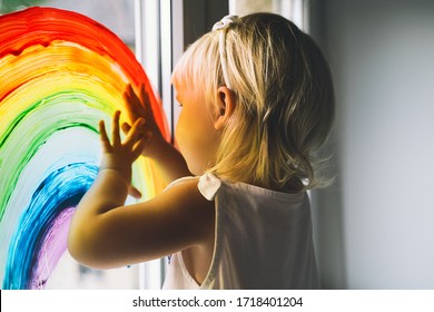 Little Girl Hands Touch Painting Rainbow On Window. Child Art And Creative. Kids Leisure At Home, Childcare, Safety Joy Symbol. Positive Visual Support During Quarantine Coronavirus Covid-19 At Home.