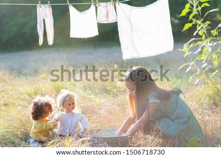 Little girl hangs out to dry retro doll clothes, summer nature outdoor. Washing, children's games, kid's leisure, vintage style.