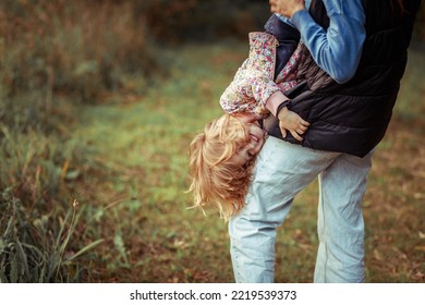 A Little Girl Hangs Upside Down In Her Mother's Arms, The Child Has Fun, Pampering, Playing With Mom, Children Lead An Active Lifestyle, Family Pastime.
