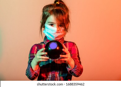 Little girl has fabric mask protect herself from Coronavirus COVID-19, child with a mask for safety. Studio shot with 8 magic prediction ball.
