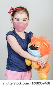 Little Girl Has Fabric Mask Protect Herself From Coronavirus COVID-19, Child With A Mask For Safety.Studio Shot With Her Toy In Mask.