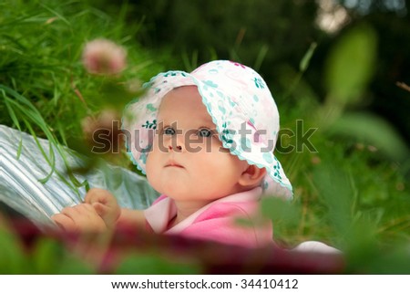 The little girl in a hat is on a grass in park in the summer