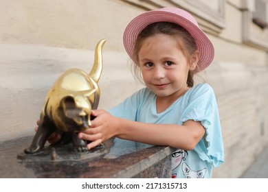 A little girl in a hat stands near the monument to the cat