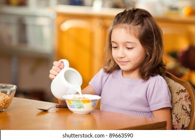 little girl having breakfast:pouring milk in the bowl