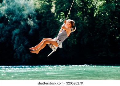 Little Girl Having Fun On Rope Swing Above River.