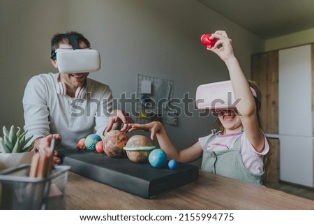 Little girl having fun time with her father using VR glasses at home for learning Solar system planets. Homeschooling concept. Modern technology using by family. Selective focus.