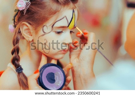 
Little Girl Having her Face Painted at a Kids Party Event. Entertainment artist creating a make-up for Halloween costume
