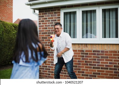 Little Girl Is Having A Water Fight In The Garden With Her Dad Using Water Pistols.