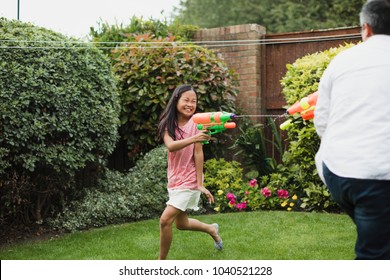 Little Girl Is Having A Water Fight In The Garden With Her Dad Using Water Pistols.