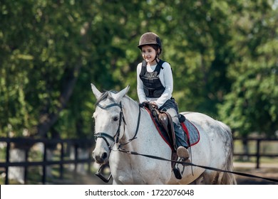 Little Girl In Helmet Learning Horseback Riding. Instructor Teaches Kid Equestrian.