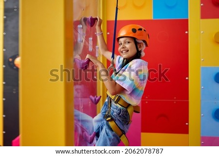 Little girl in helmet poses on climbing wall