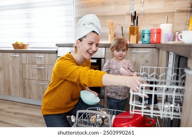 Little girl helping her mum load the dishwasher in the kitchen - Powered by Shutterstock