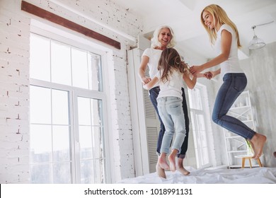 Little girl, her attractive mother and charming grandmother are having fun and jumping on bed while spending time together at home. Women's generation. International Women's Day. Happy Mother's Day.