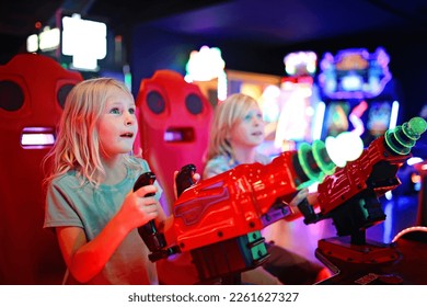 A little girl and her brother are playing an alien shooting game challenge at a neon light video arcade. - Powered by Shutterstock